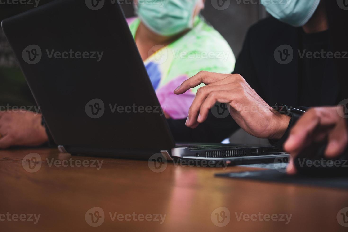 Two people talking in office and working by computer notebooks wearing masks to protect against covid-19 photo