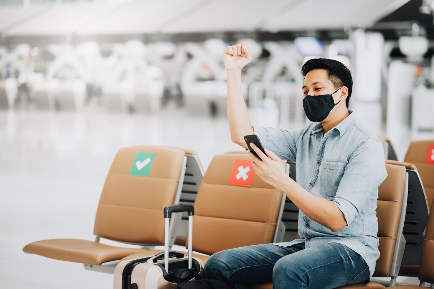 Asian man wearing face mask using mobile phone and raising his arm up to celebrate photo