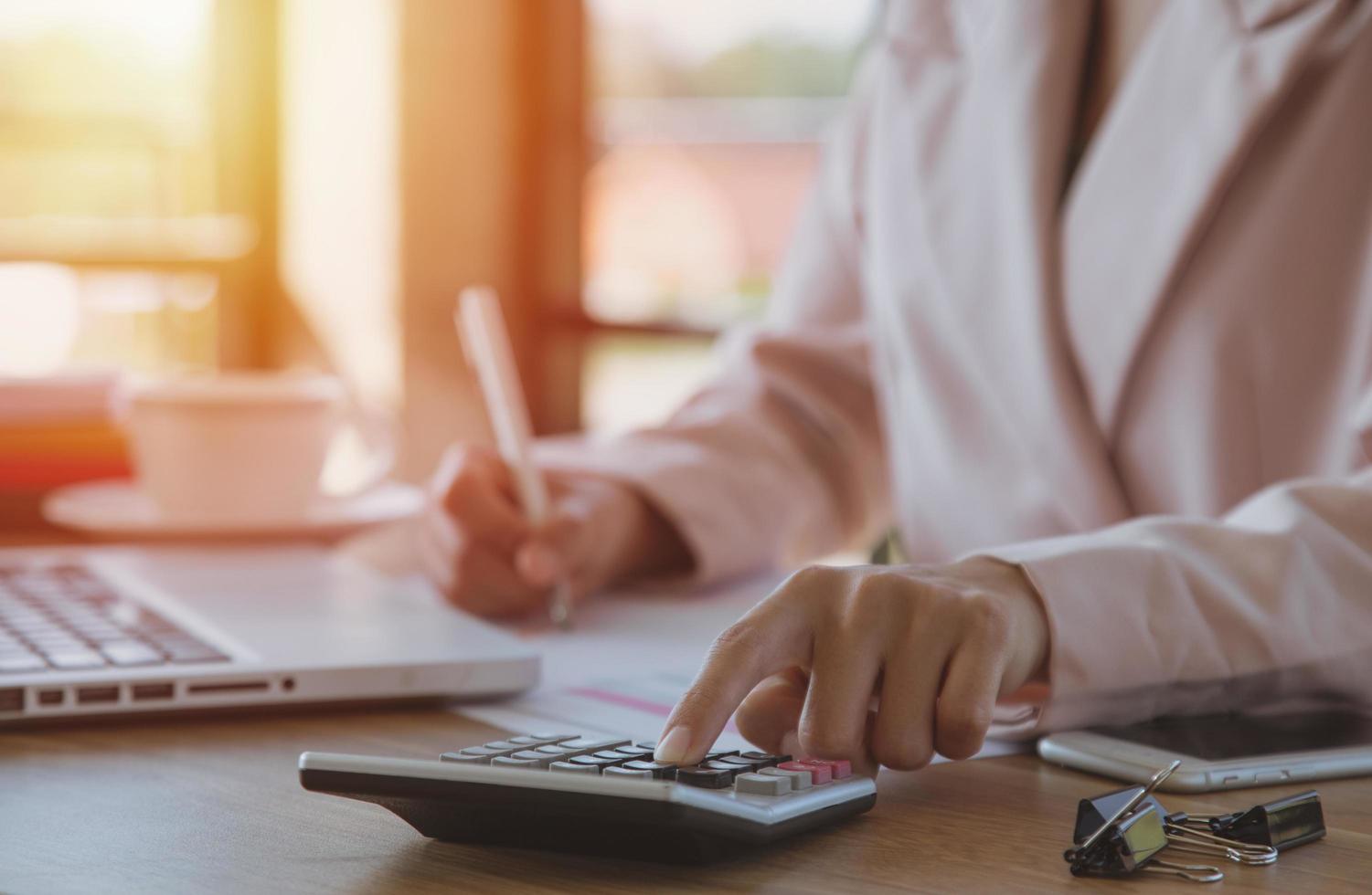 Young businesswoman using calculator working on laptop at her workstation photo