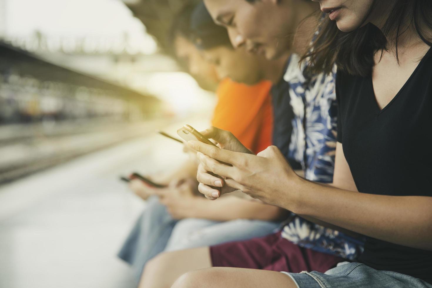 Grupo de amigos que usan teléfonos inteligentes en una estación de tren. foto