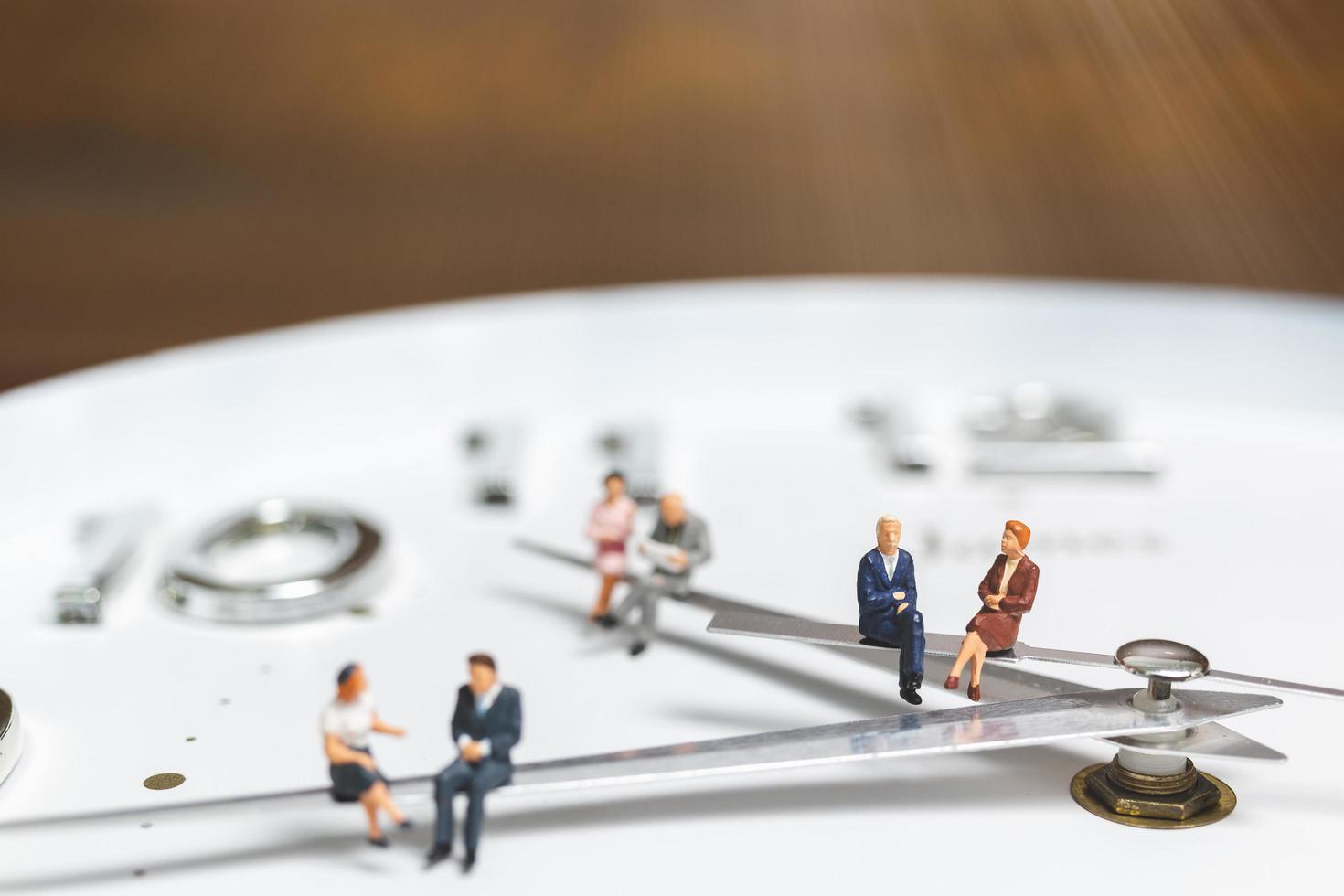 Miniature businesspeople sitting on a clock, concept of time and work photo