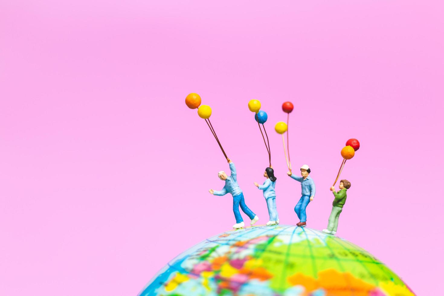 Miniature family holding balloons on a globe with a pink background photo