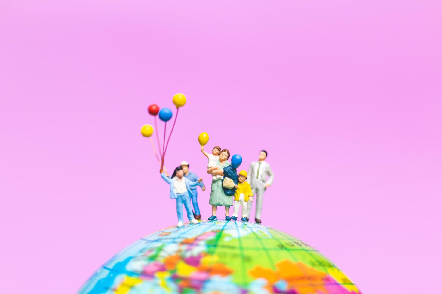 Familia en miniatura sosteniendo globos en un globo con un fondo rosa foto