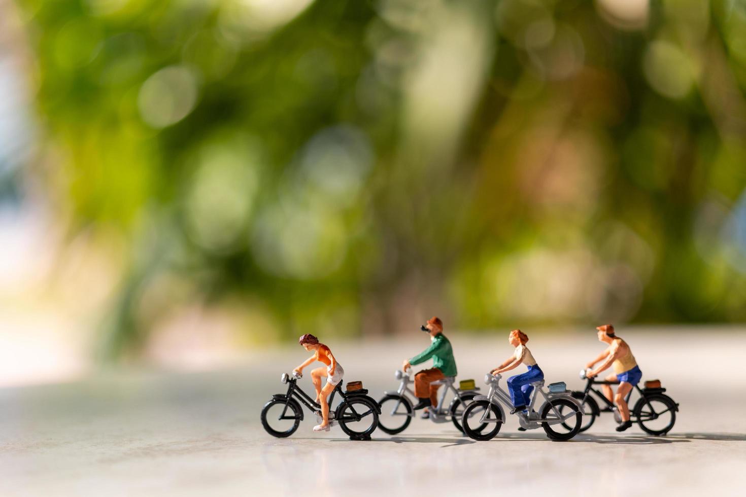 Miniature people riding bicycles outdoors with a green bokeh background, sport and travel  concept photo