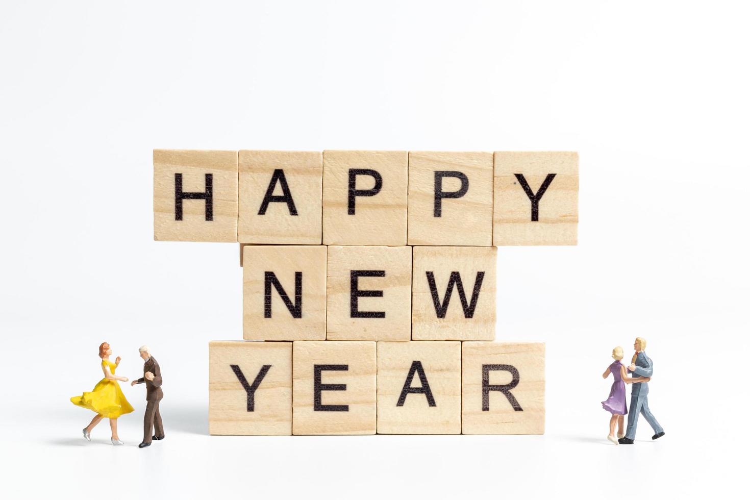 Gente en miniatura bailando sobre bloques de madera con el texto feliz año nuevo sobre un fondo blanco. foto