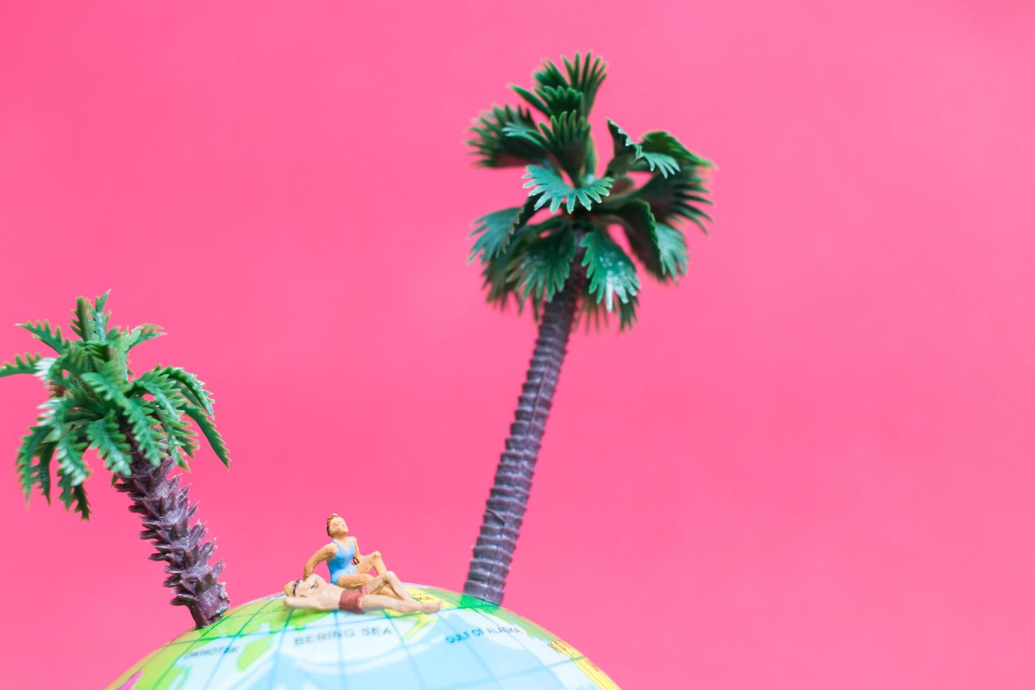 Miniature people wearing swimsuits relaxing on a globe with a pink background, honeymoon concept photo