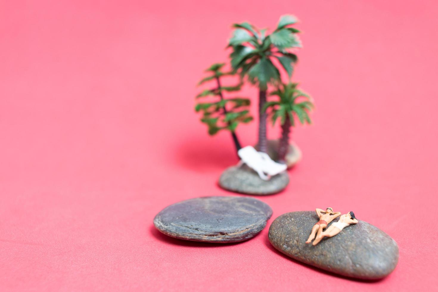 Miniature people wearing swimsuits relaxing on a rock with a pink background photo