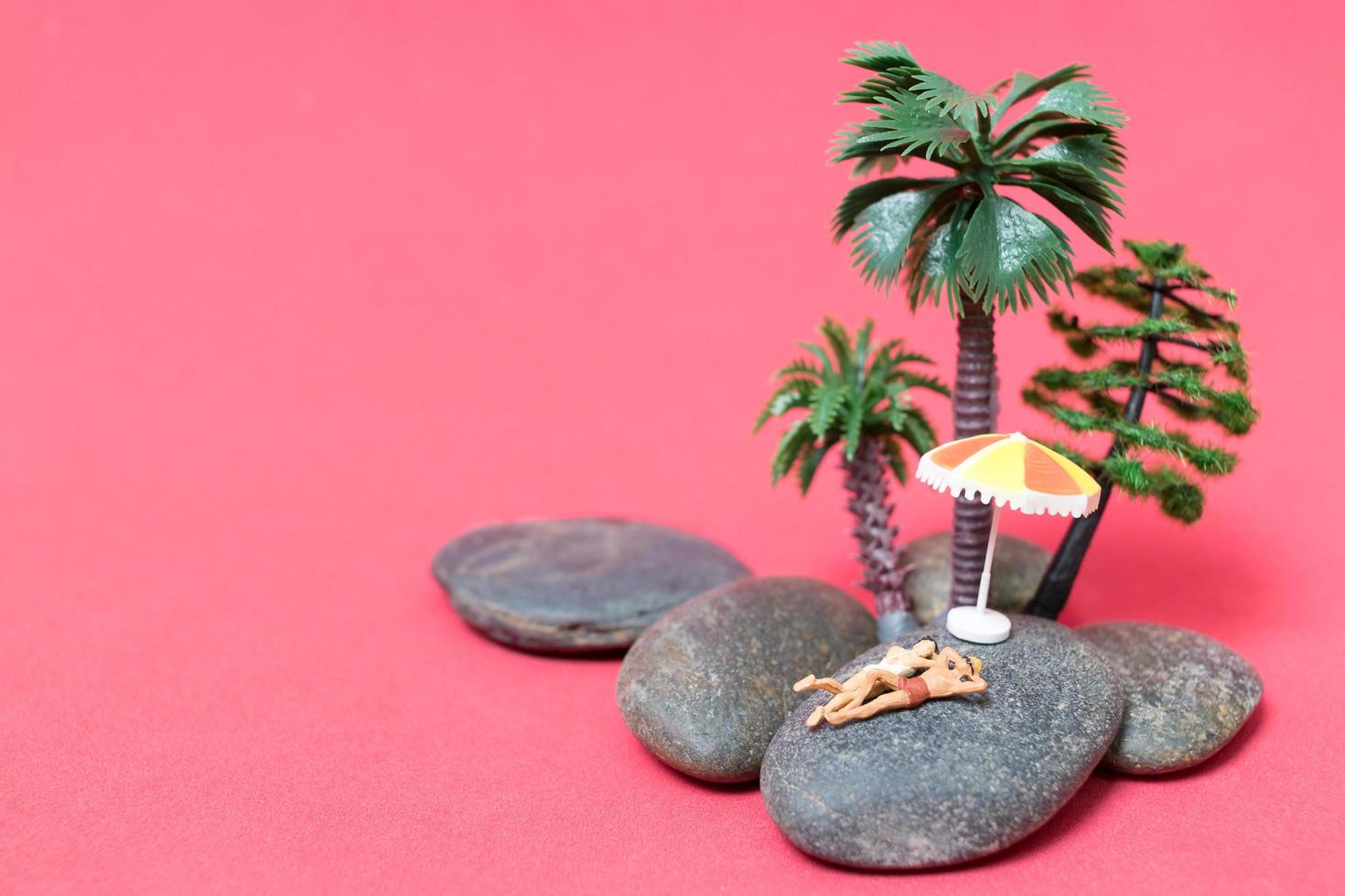 Miniature people wearing swimsuits relaxing on a rock with a pink background photo