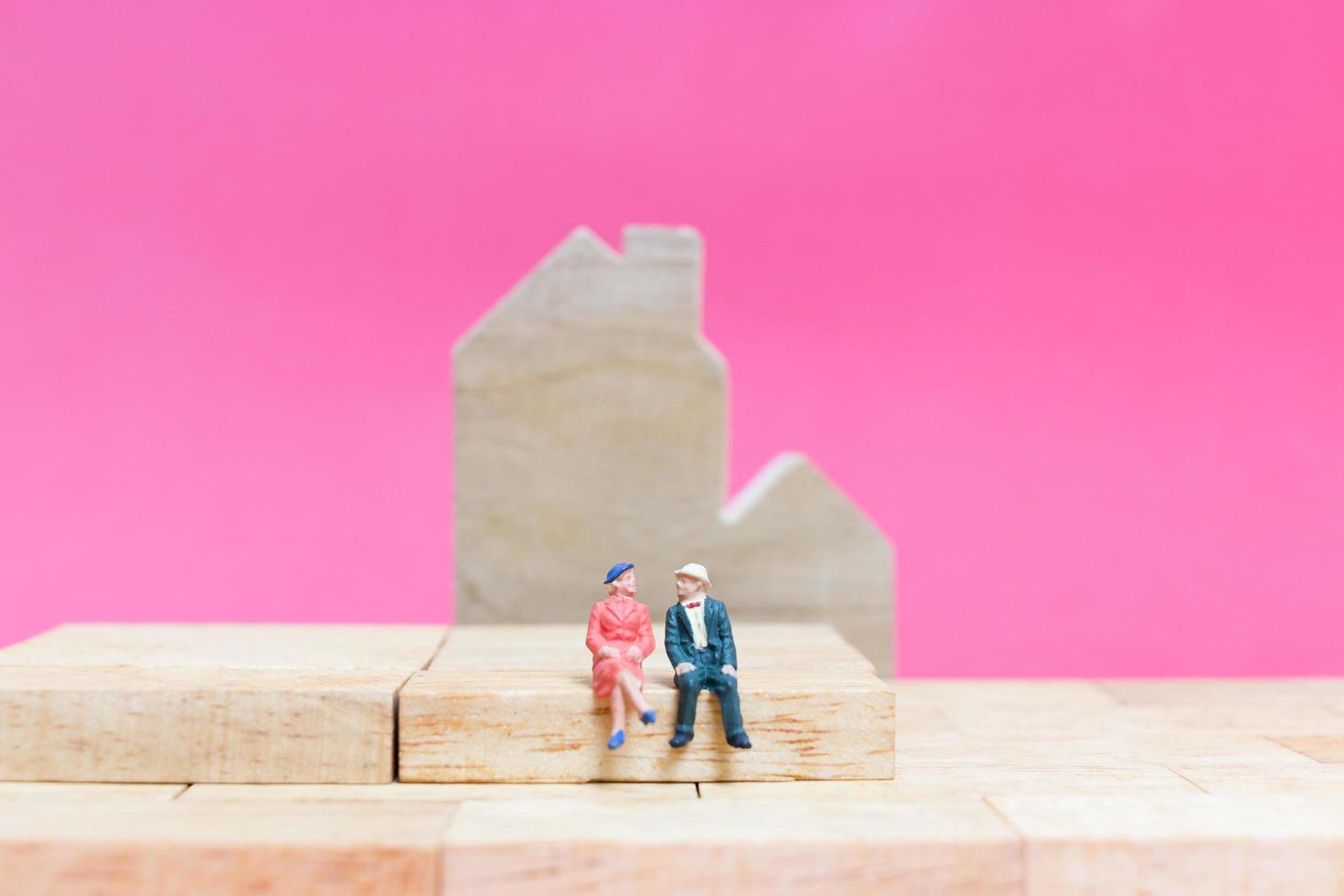 Pareja en miniatura con casas sobre un fondo rosa, concepto de día de San Valentín foto