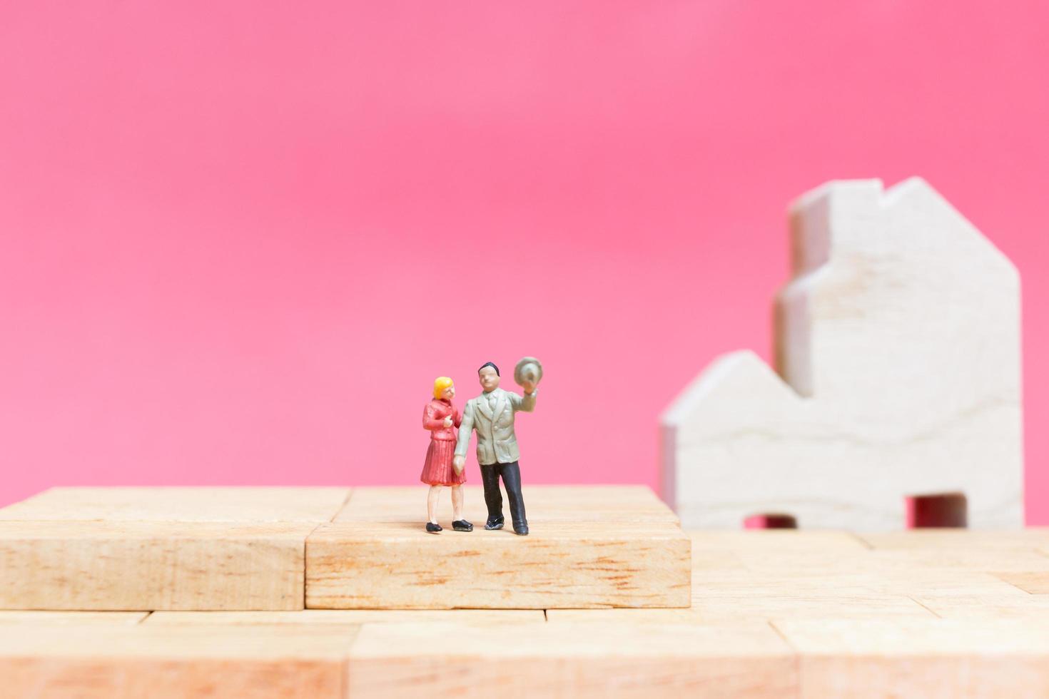 Pareja en miniatura con casas sobre un fondo rosa, concepto de día de San Valentín foto