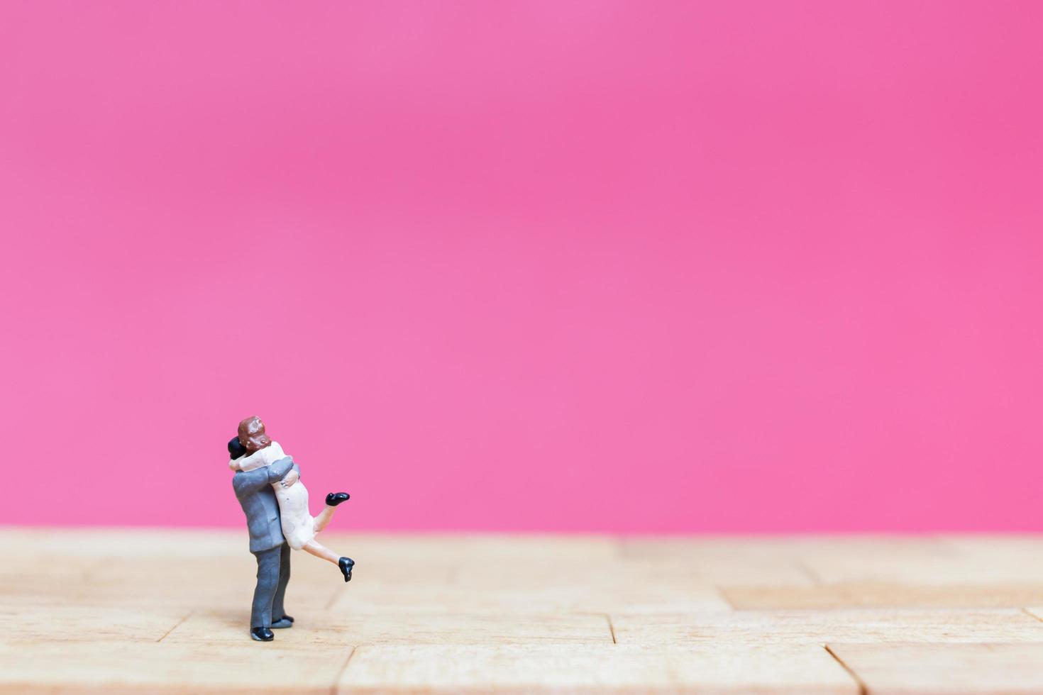 Pareja en miniatura abrazándose sobre un fondo rosa, concepto de día de San Valentín foto