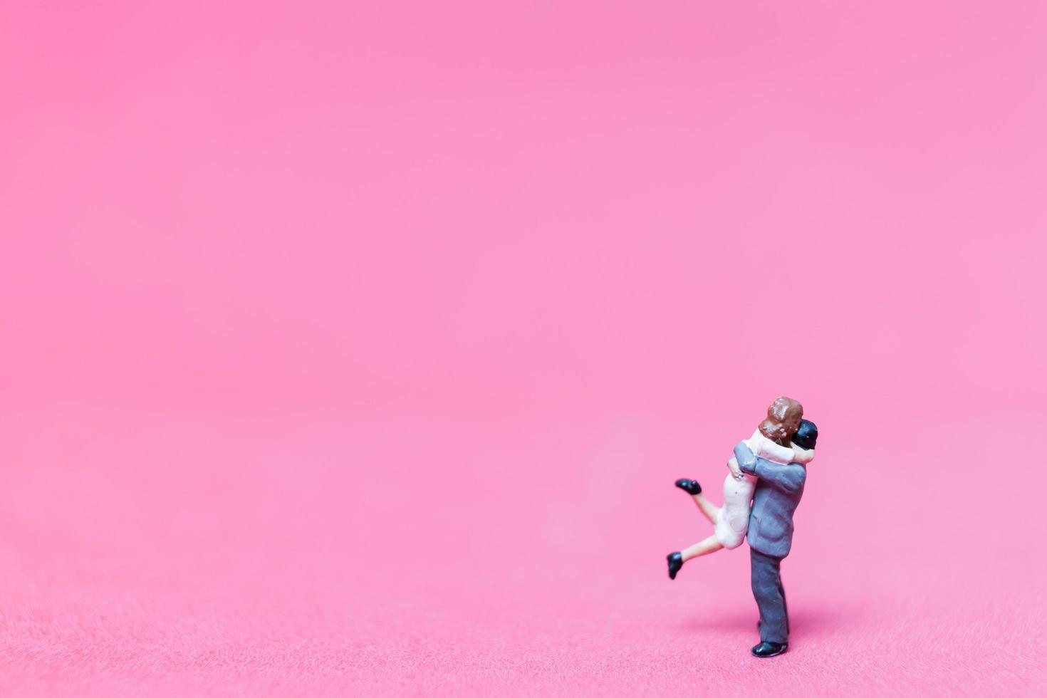 Pareja en miniatura abrazándose sobre un fondo rosa, concepto de día de San Valentín foto