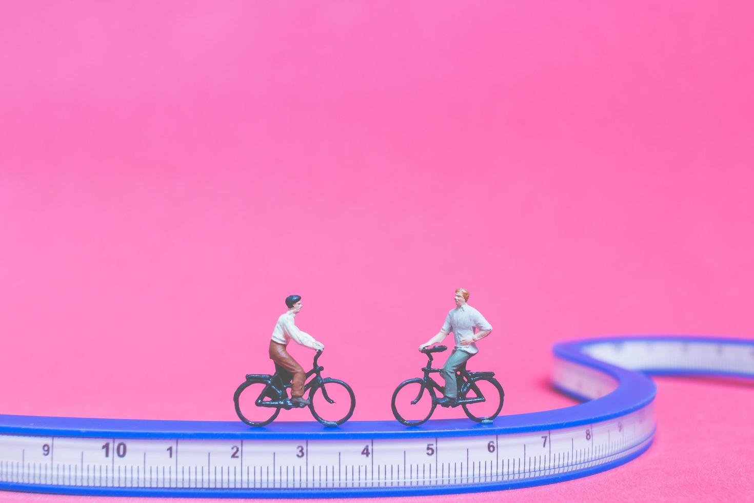 Viajeros en miniatura con bicicletas en un puente azul sobre un fondo de color rosa foto