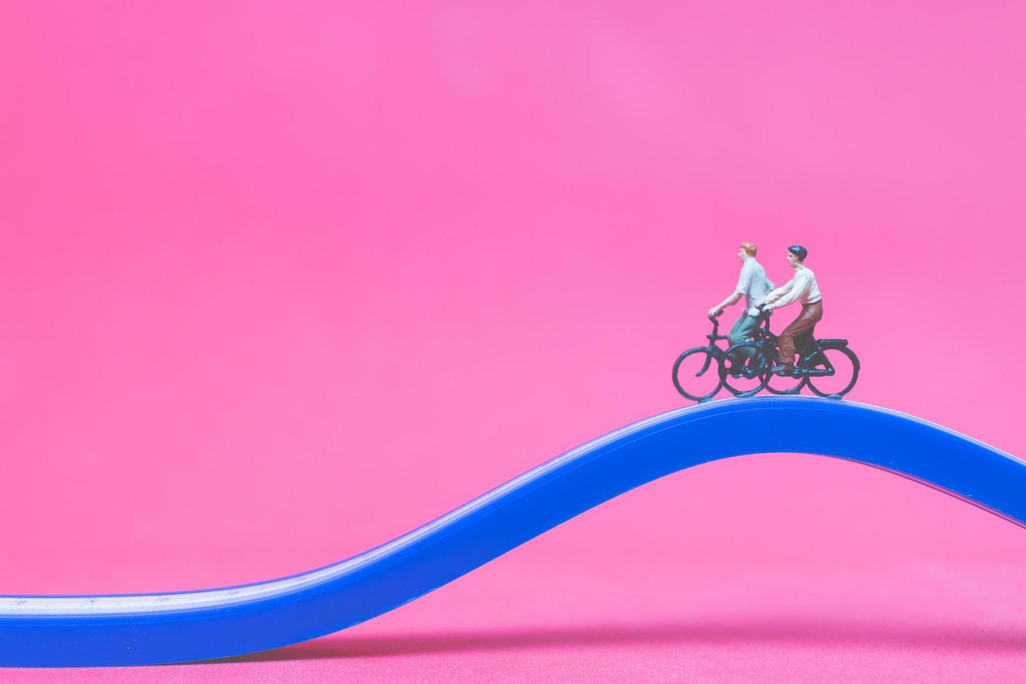 Viajeros en miniatura con bicicletas en un puente azul sobre un fondo de color rosa foto