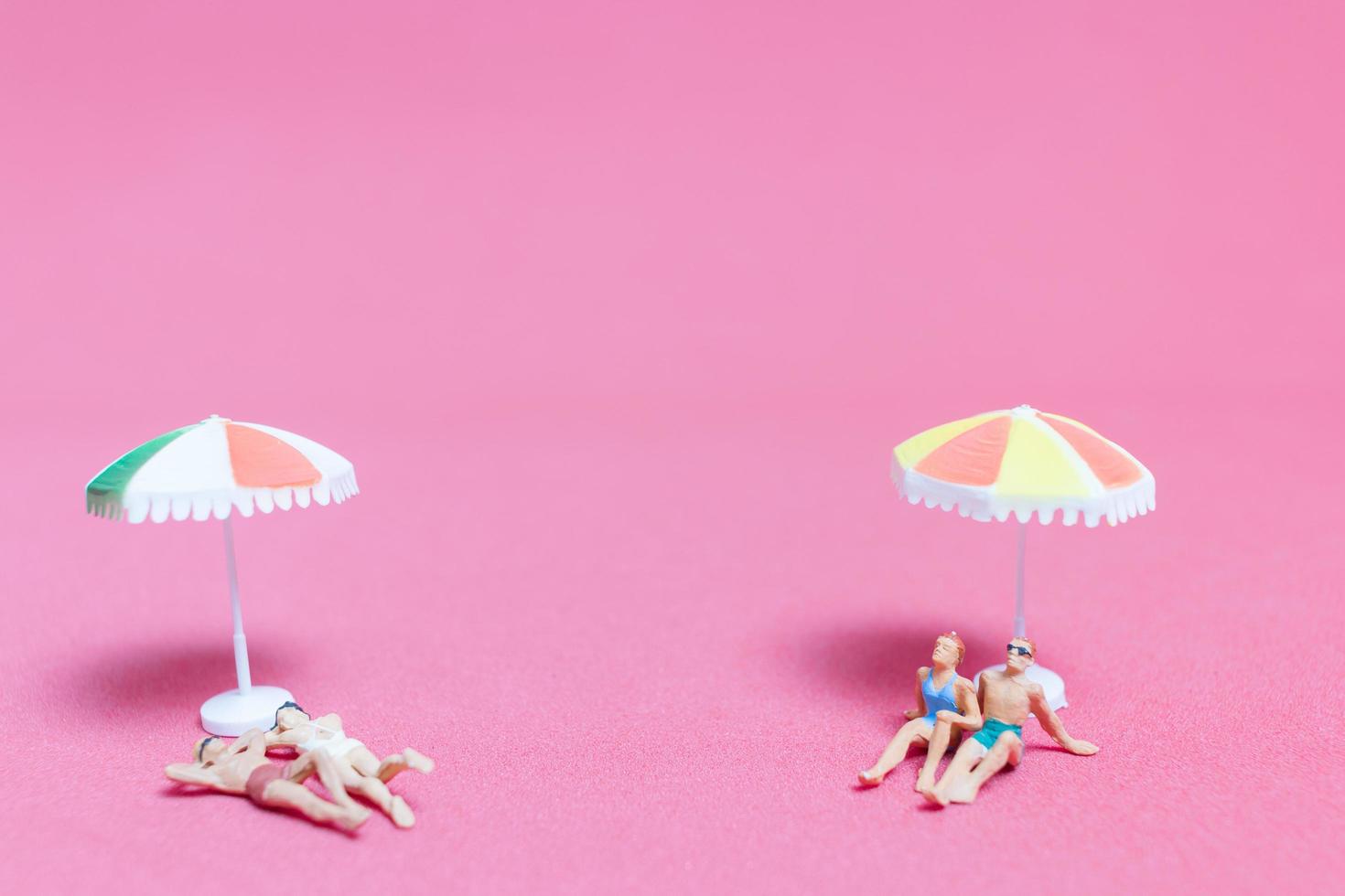 Gente en miniatura vistiendo trajes de baño relajándose sobre un fondo de color rosa foto