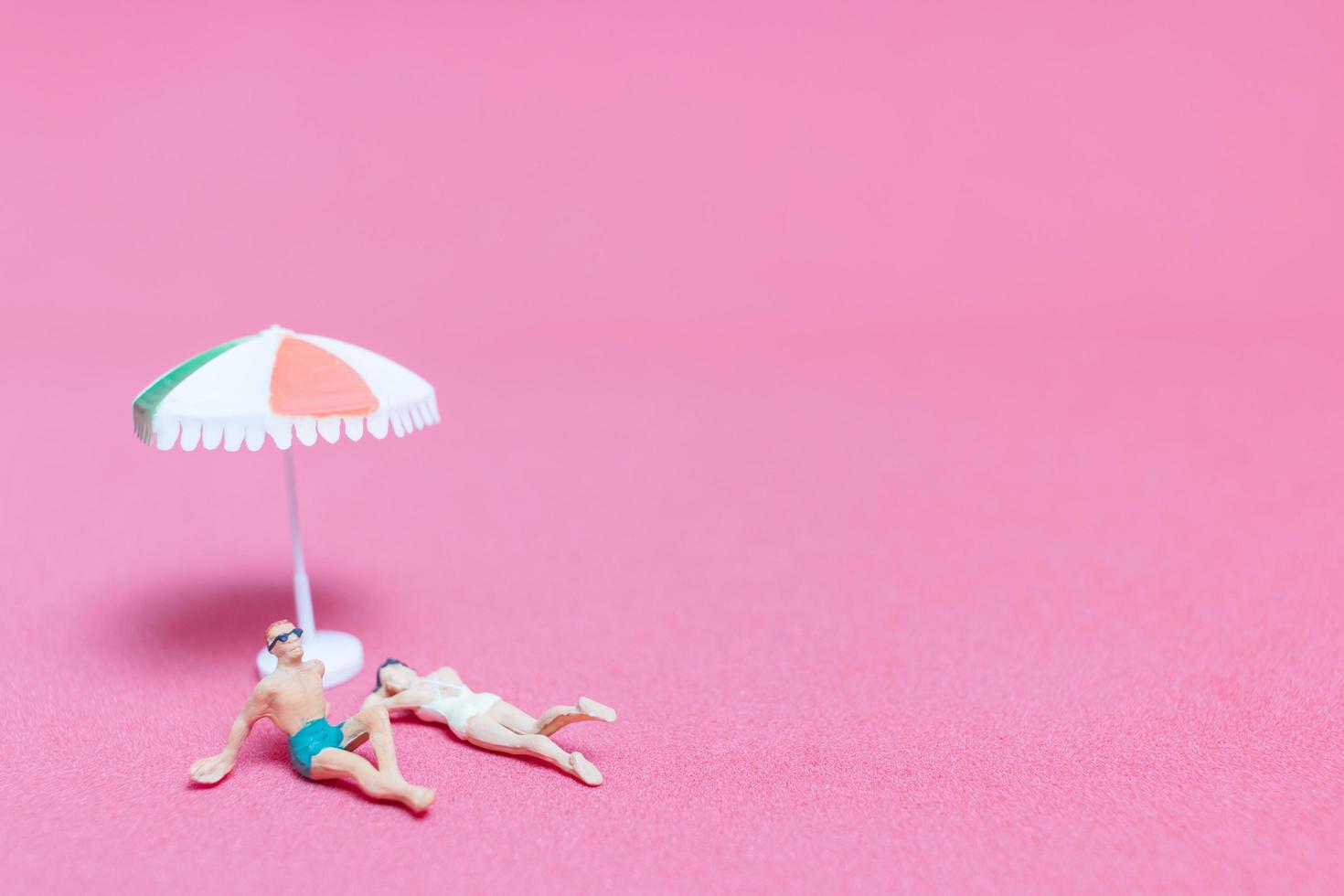 Miniature people wearing swimsuits relaxing on a pink background photo