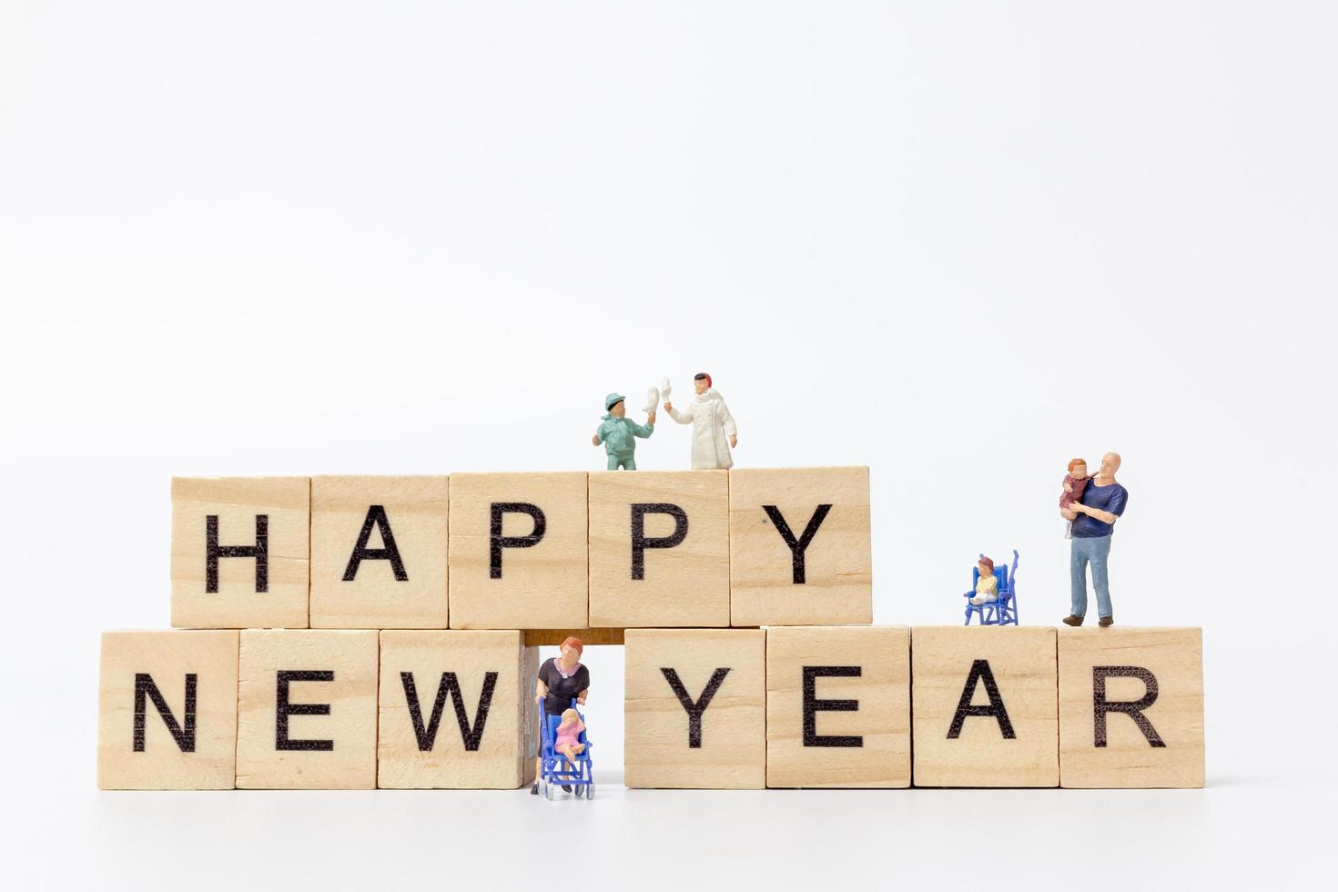 Familias en miniatura sobre bloques de madera con el texto feliz año nuevo sobre un fondo blanco. foto