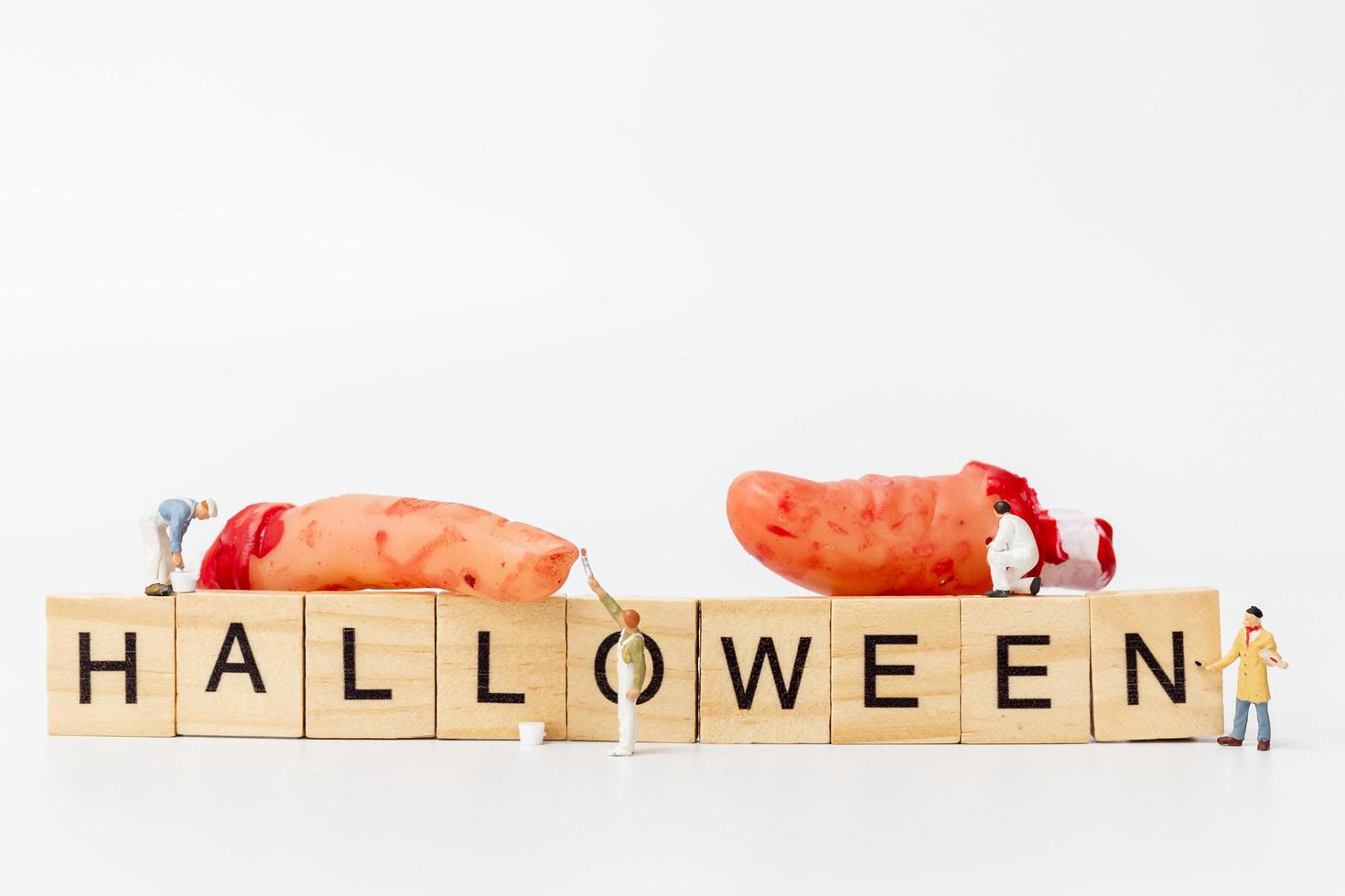 Trabajadores en miniatura que se unen para crear accesorios de fiesta de Halloween con bloques de madera con el texto Halloween sobre un fondo blanco. foto