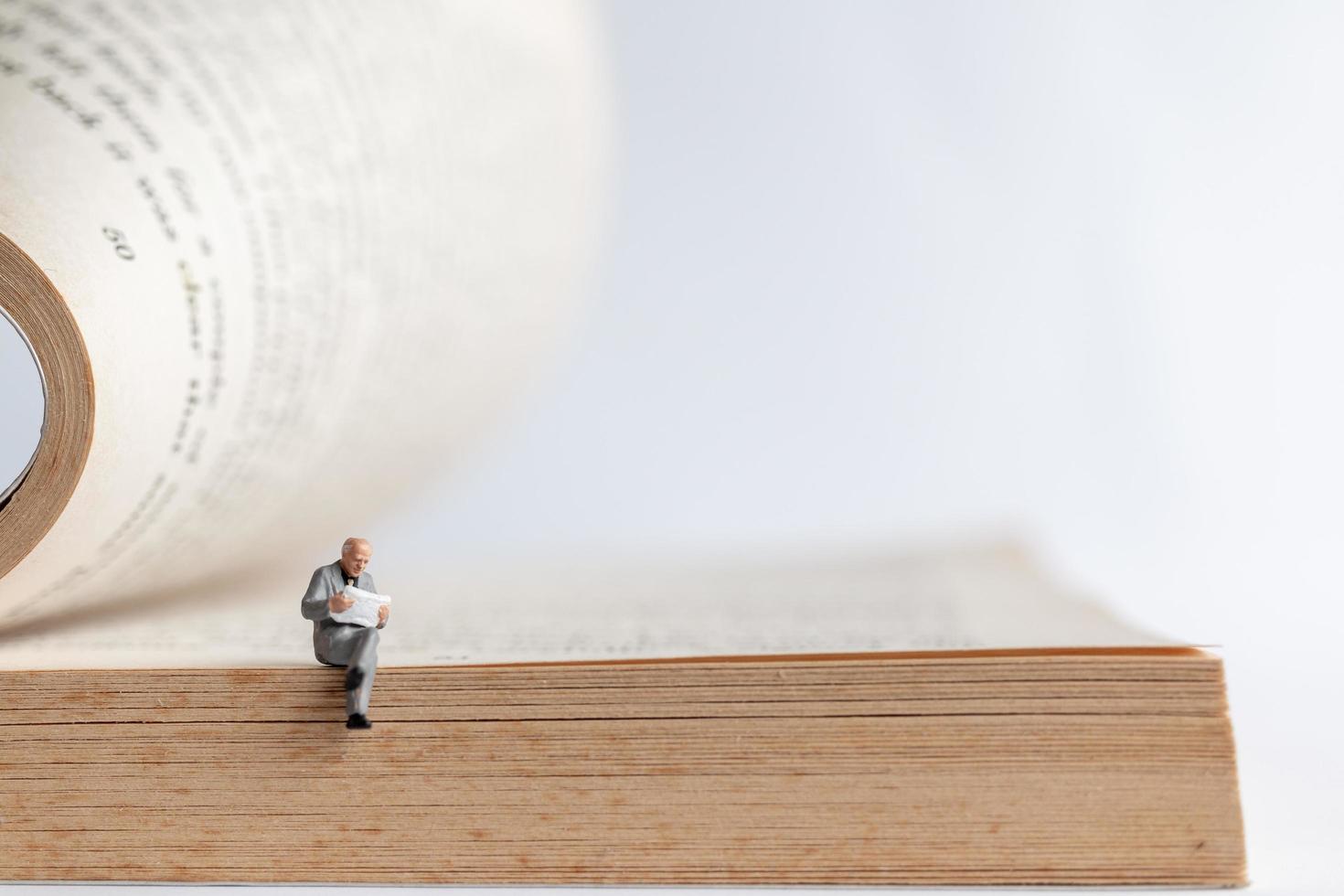 Empresario en miniatura leyendo un libro sobre un libro antiguo, concepto de educación empresarial foto