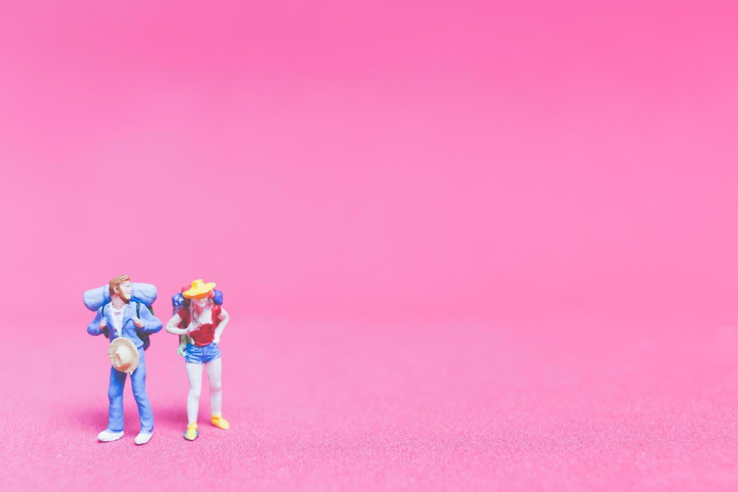 Pareja de viajeros en miniatura sobre un fondo de color rosa foto