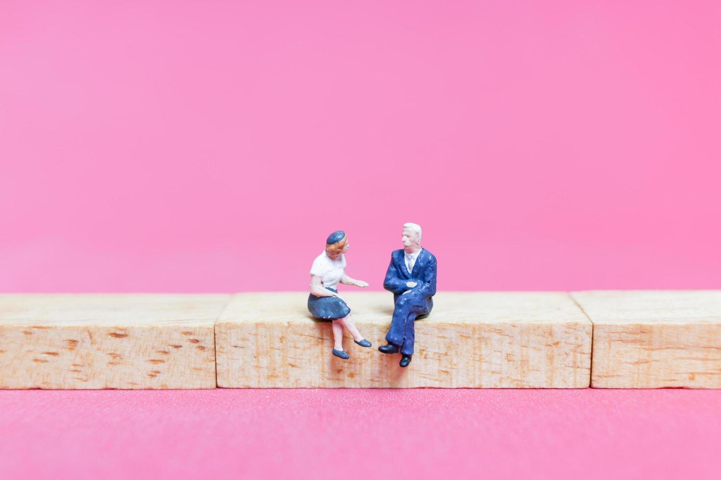 Miniature couple sitting on wooden blocks on a pink background photo