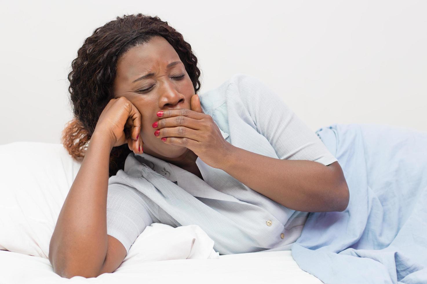 Young African woman yawns lying in bed at home photo