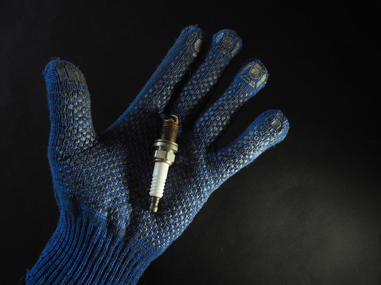 A faulty car spark plug in a man's blue work glove against a black background photo