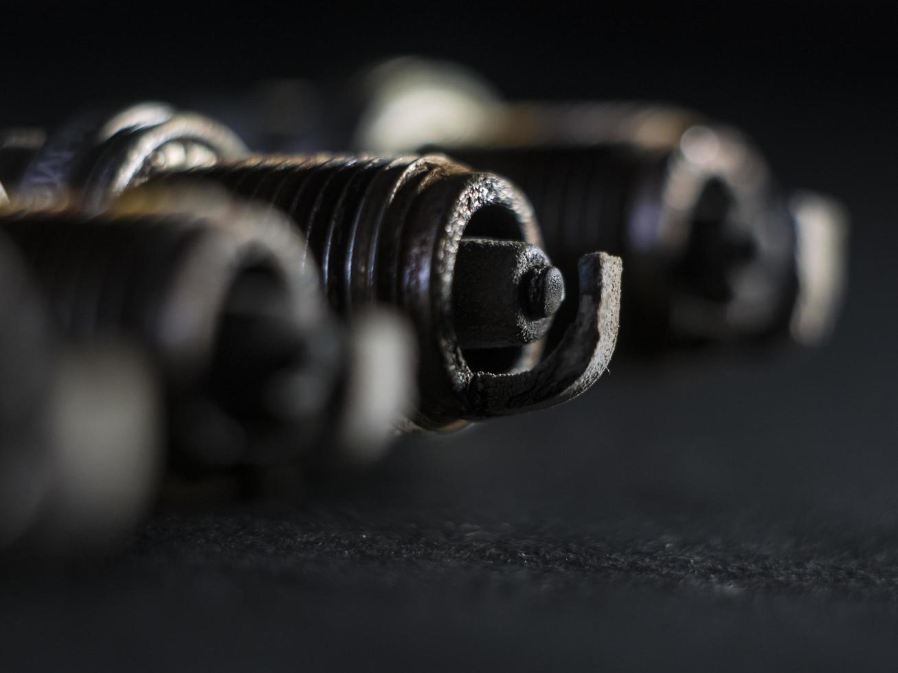 A close-up of a car's faulty spark plugs, against a black background photo