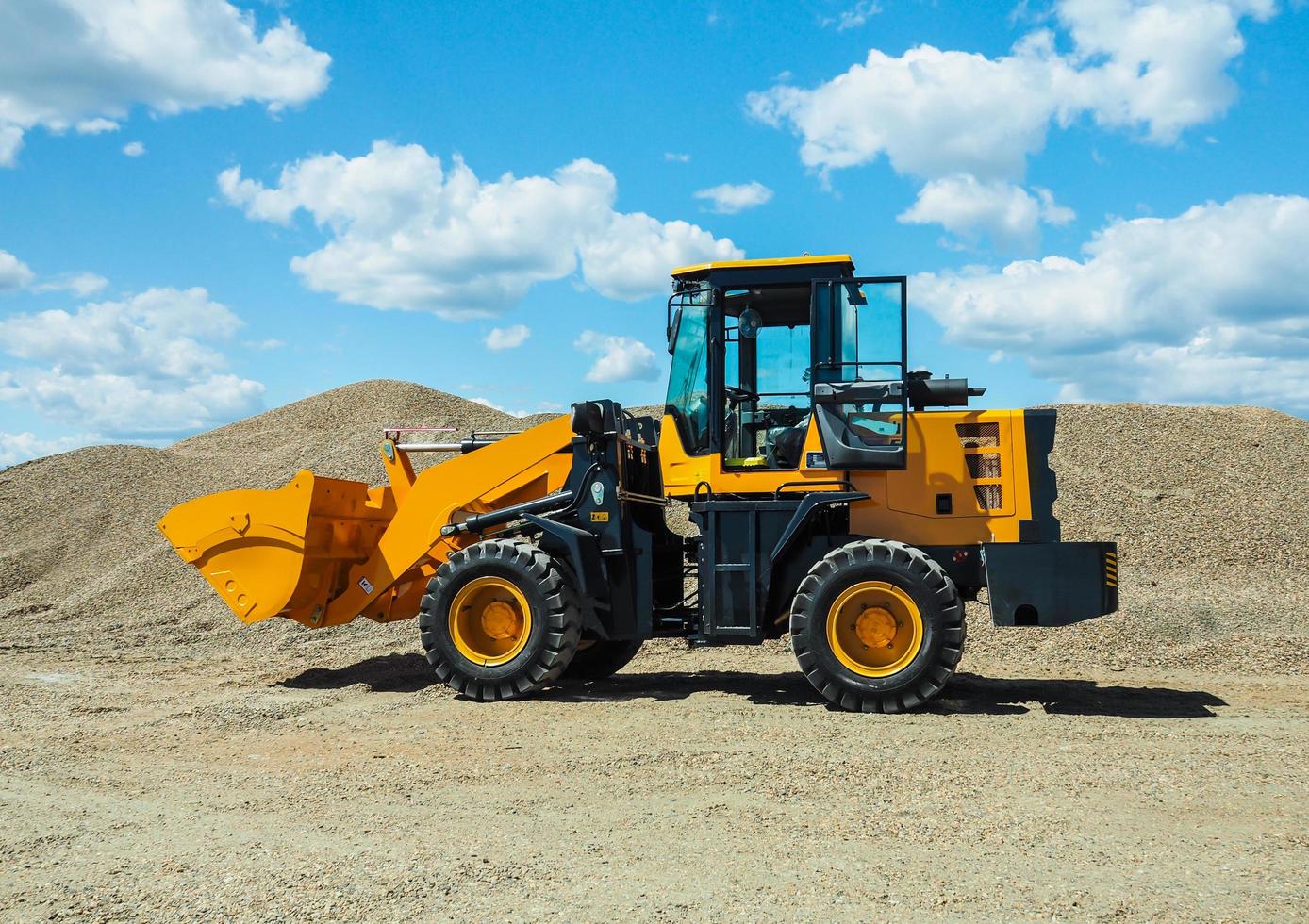 Black-yellow front loader with small wheels against the background of a large pile of stone sand photo