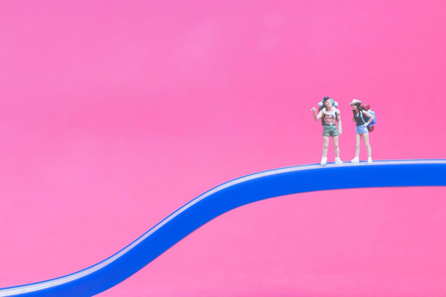 Pareja de viajeros en miniatura en un puente con un fondo de color rosa foto