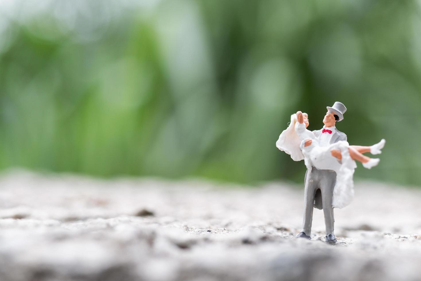 Miniature bride and groom standing outdoors with a blurry nature background photo