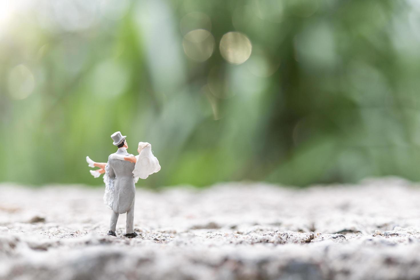 Miniature bride and groom standing outdoors with a blurry nature background photo