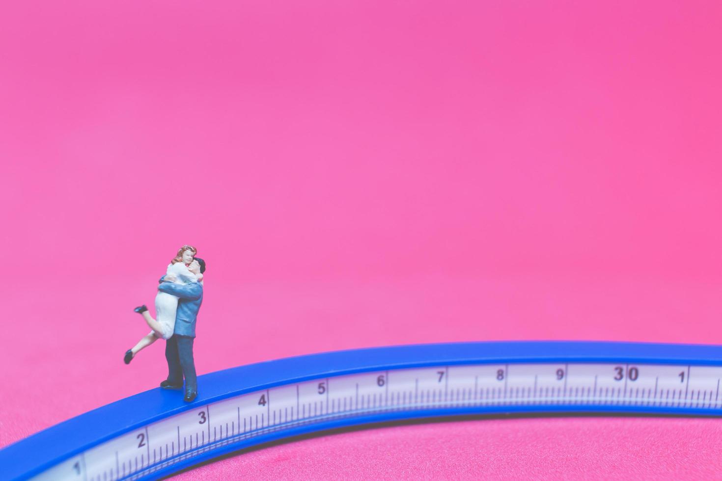 Pareja en miniatura abrazándose en un puente con un fondo de color rosa foto