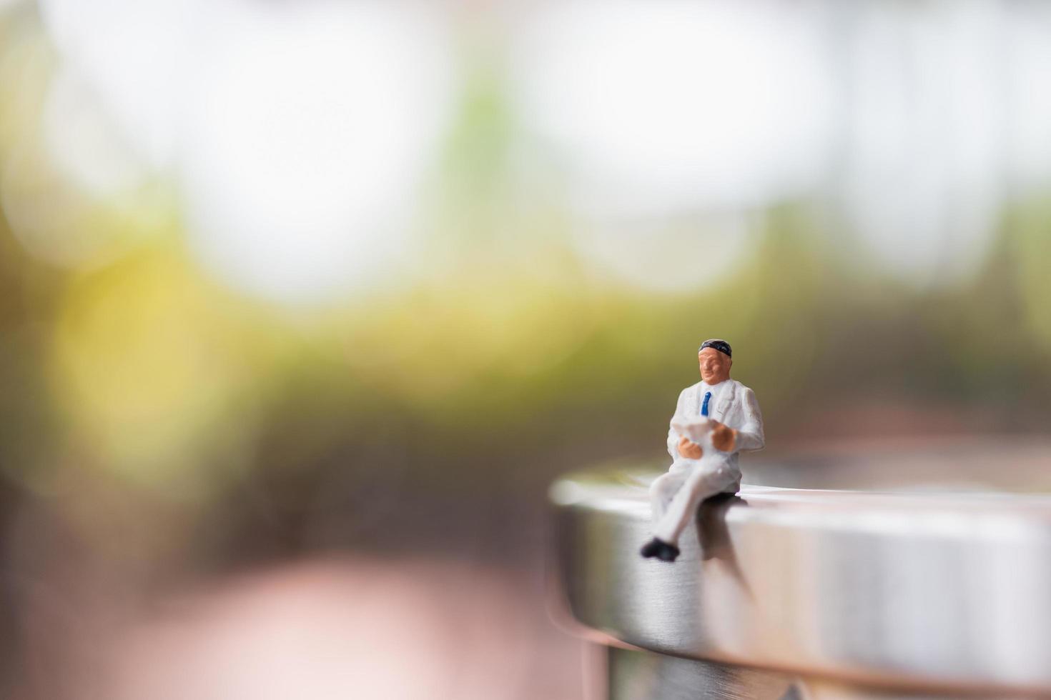 Empresario en miniatura sentado y leyendo un libro al aire libre, la educación y el concepto empresarial foto