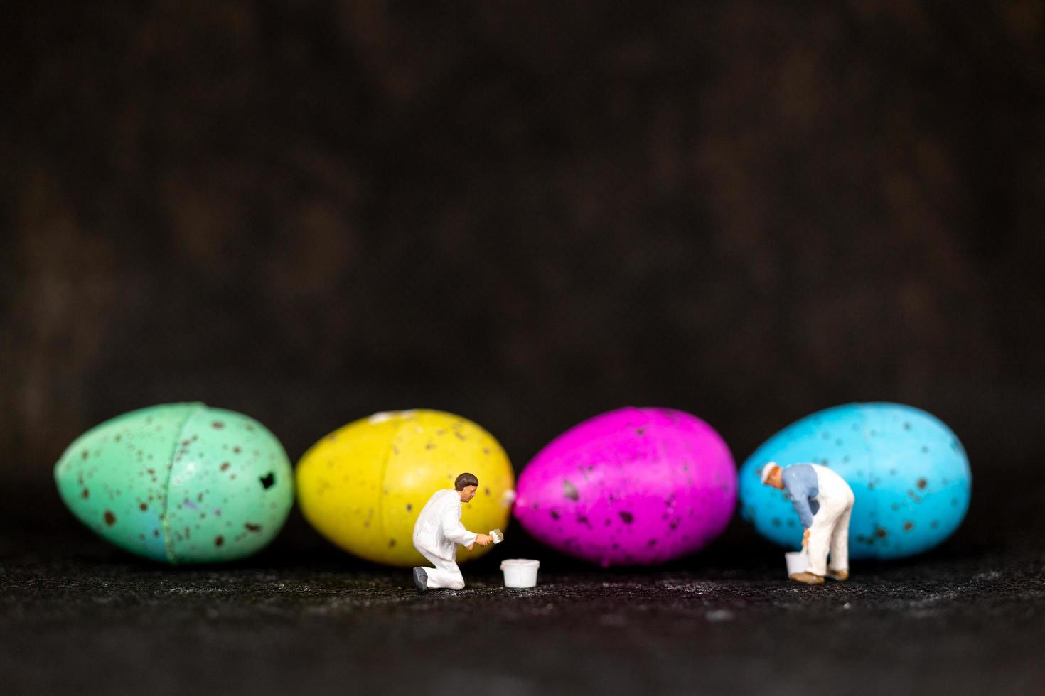 Gente en miniatura pintando huevos de pascua para el día de pascua sobre un fondo negro foto