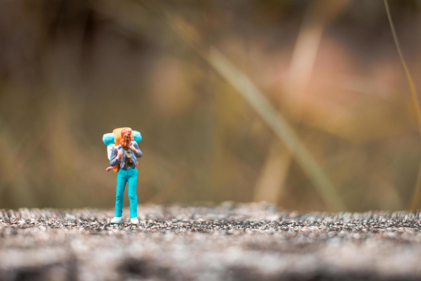 Miniature backpacker standing on a concrete floor with a bokeh nature background photo