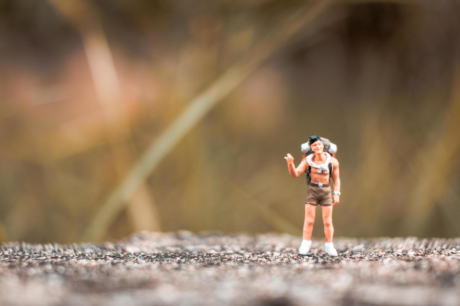 Miniature backpacker standing on a concrete floor with a bokeh nature background photo