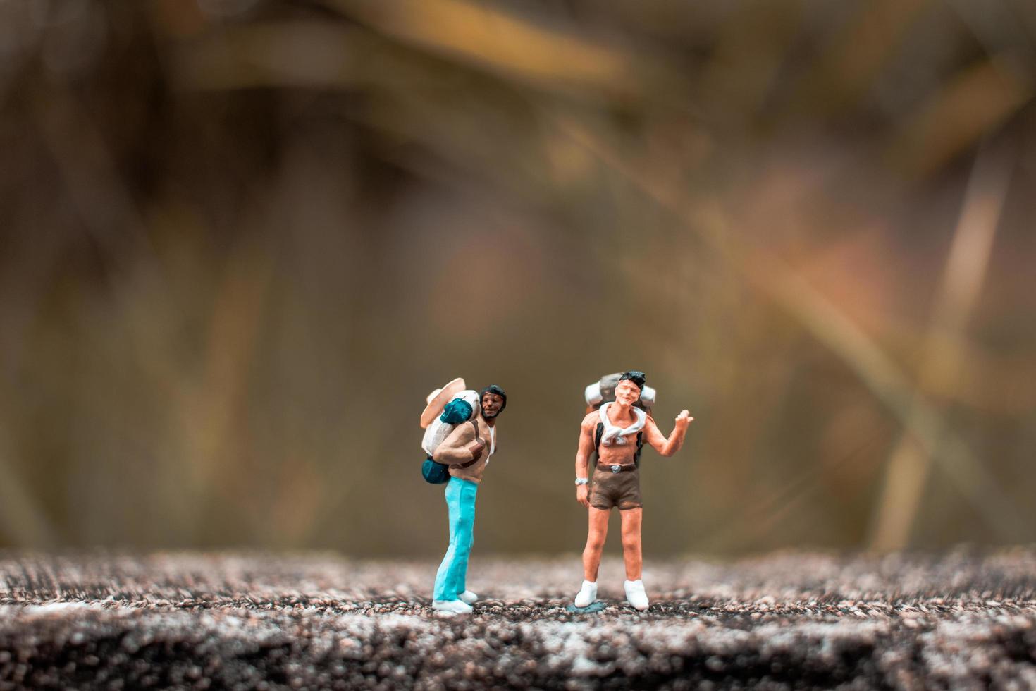 Miniature backpackers standing on a concrete floor with a bokeh nature background photo