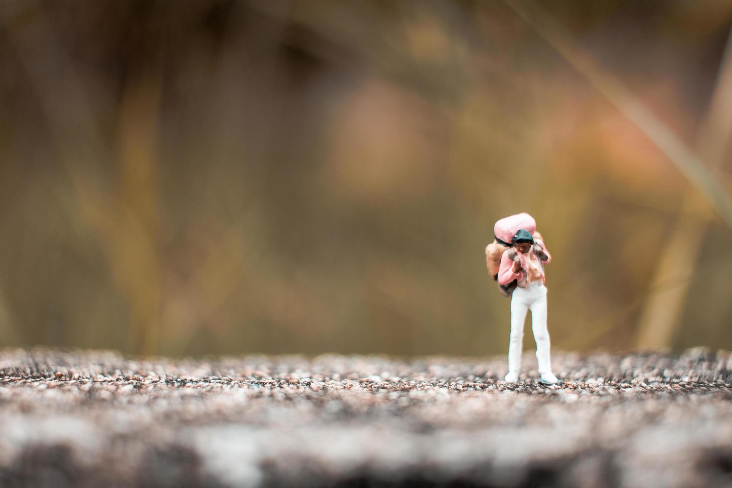 Miniature backpacker standing on a concrete floor with a bokeh nature background photo