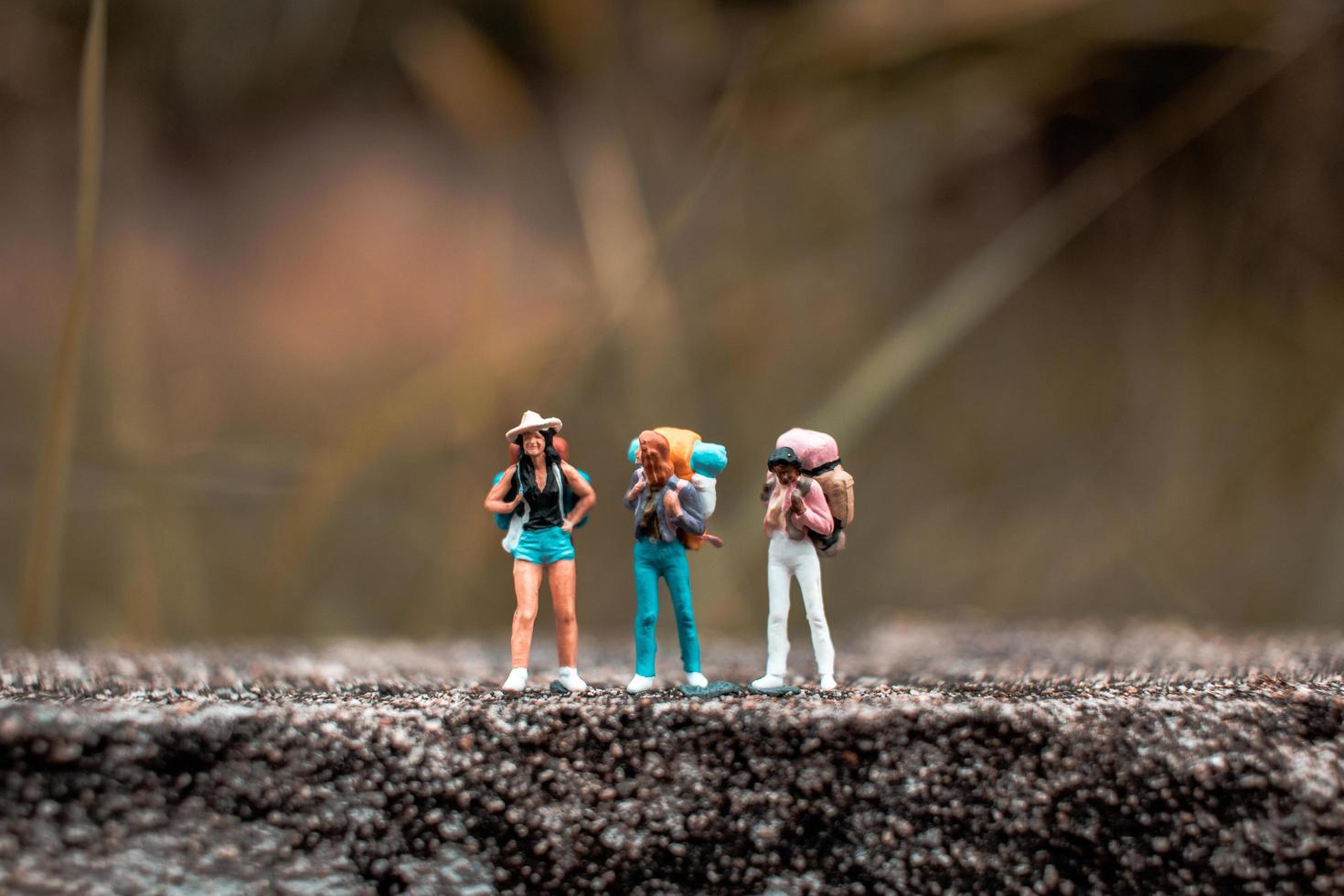 Miniature backpackers standing on a concrete floor with a bokeh nature background photo