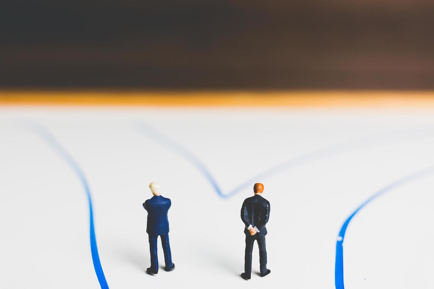 Miniature businessmen standing on an arrow pathway, business decision concept photo