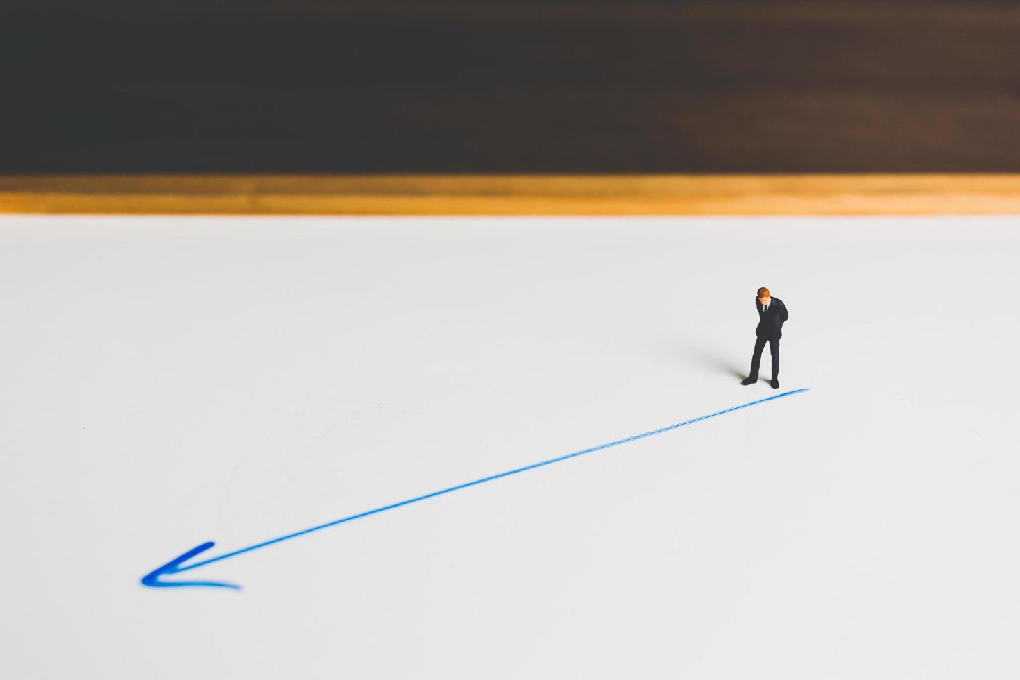 Miniature businessman standing on an arrow pathway, business decision concept photo