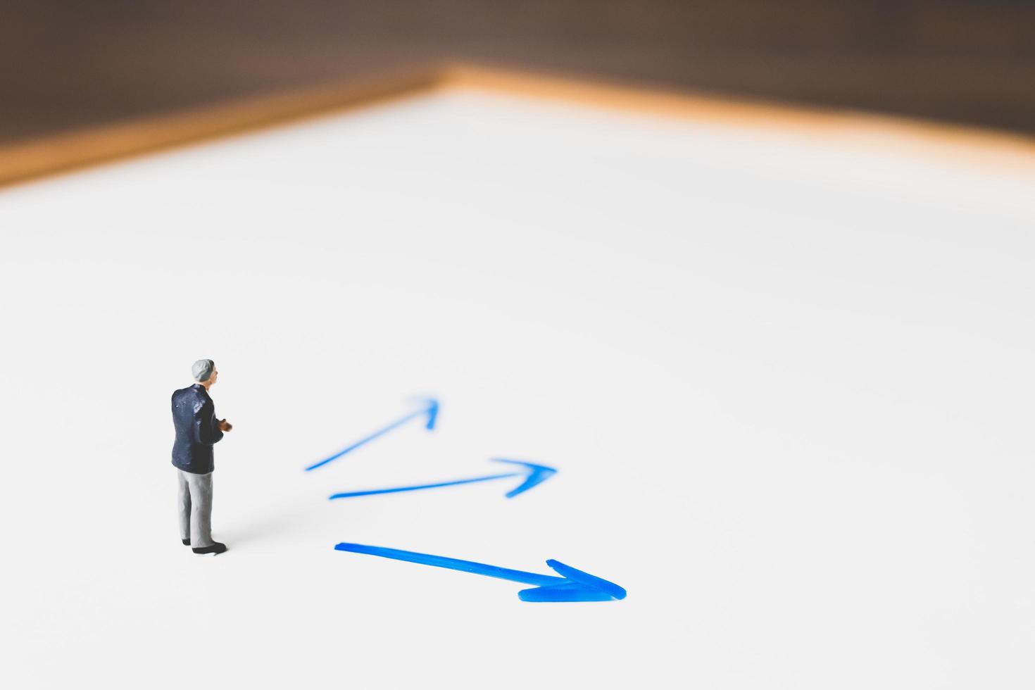 Miniature businessman standing on an arrow pathway, business decision concept photo