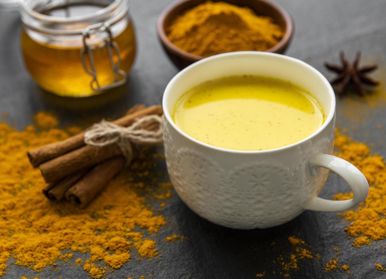 Golden milk with cinnamon, turmeric, ginger and honey over black concrete background photo