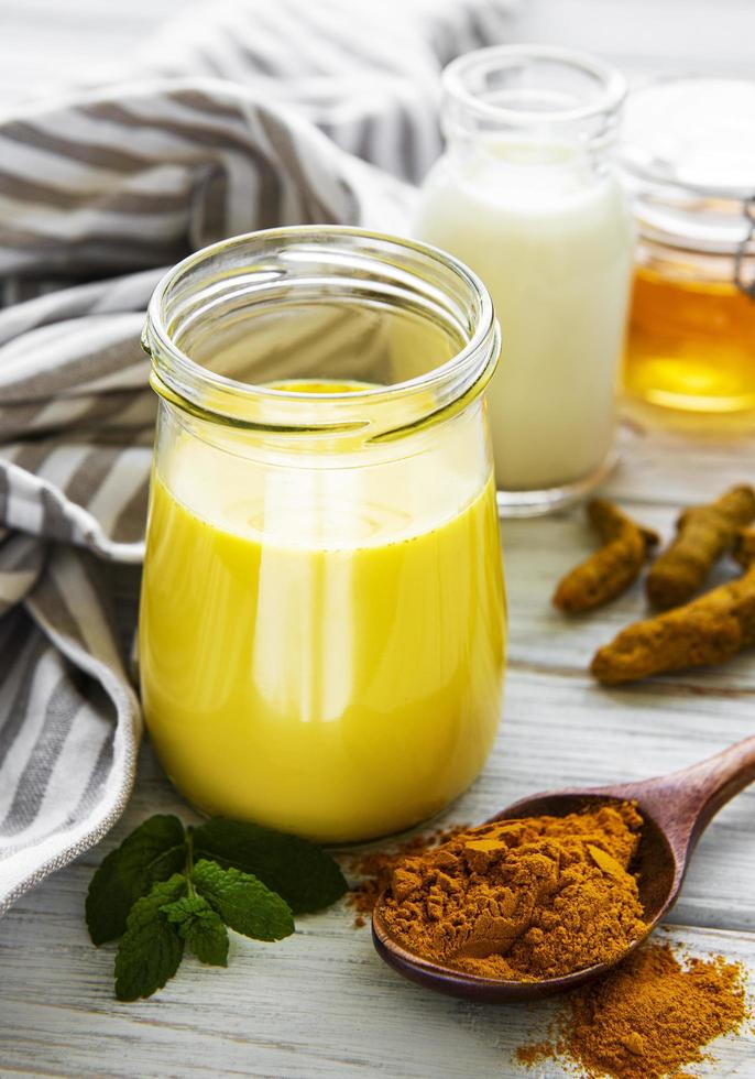 Leche dorada con canela, cúrcuma, jengibre y miel sobre fondo de madera blanca foto