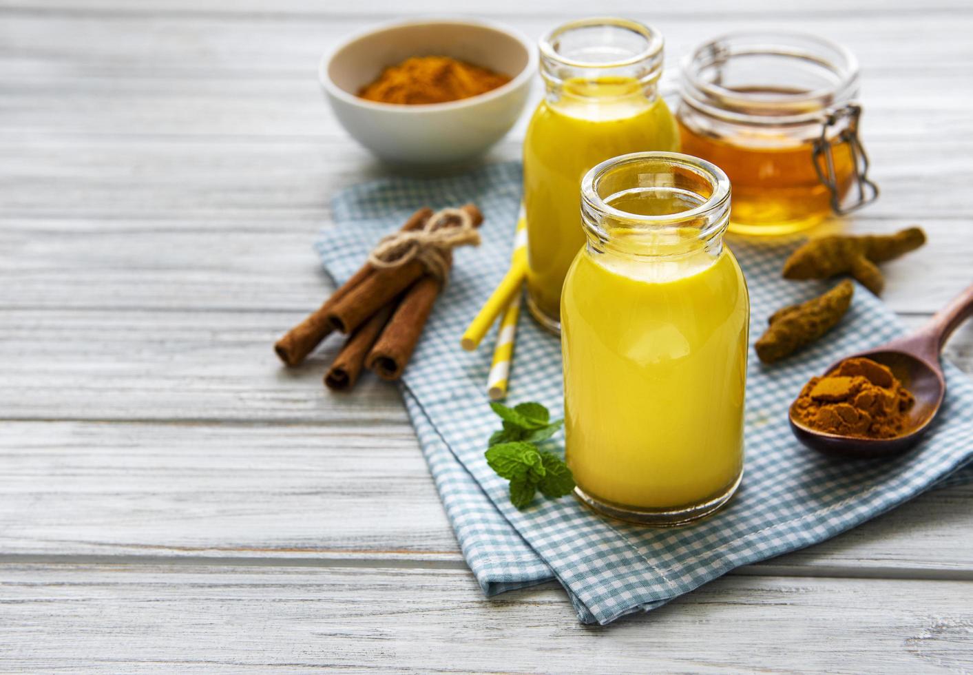 Golden milk with cinnamon, turmeric, ginger and honey over white wooden background photo