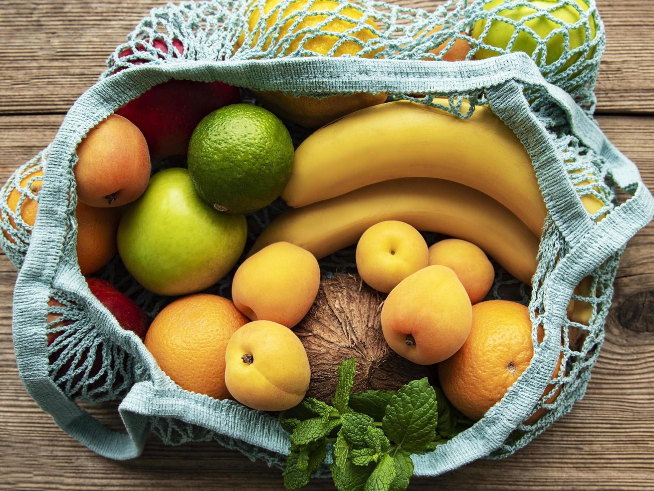 Bolsa de malla con frutas orgánicas sobre fondo de madera foto