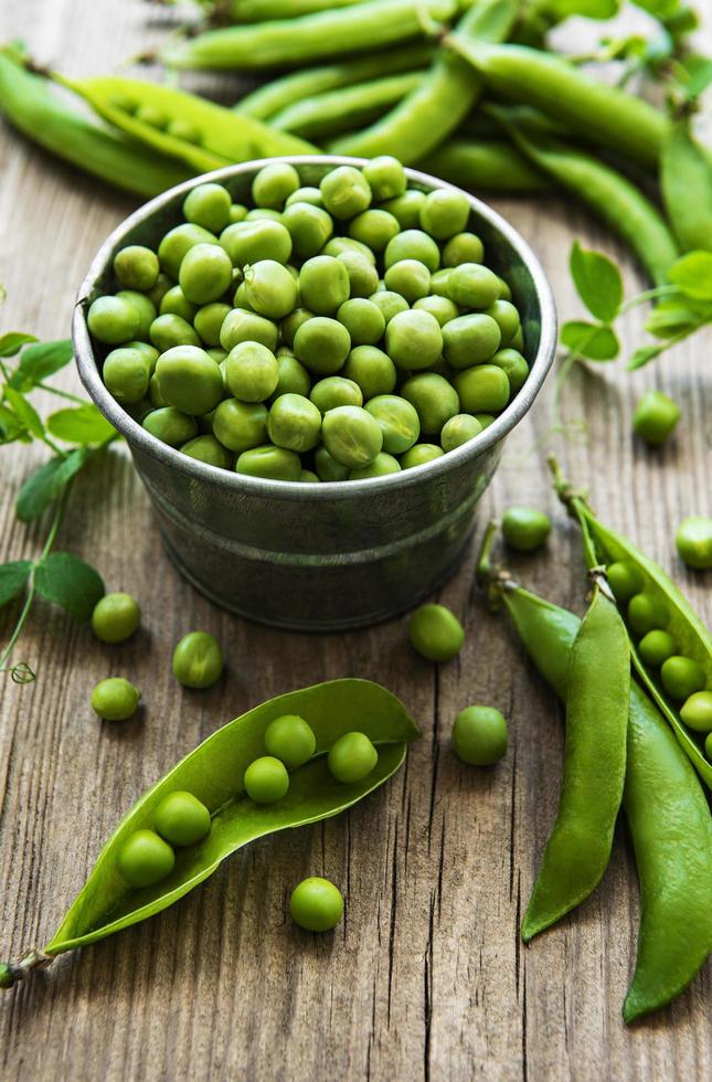 Fresh green peas in a small metal bucket on old wooden background photo