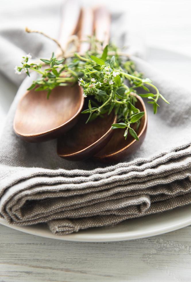 cucharas de madera en un plato y servilletas de lino decoradas con ramos verdes de tomillo foto