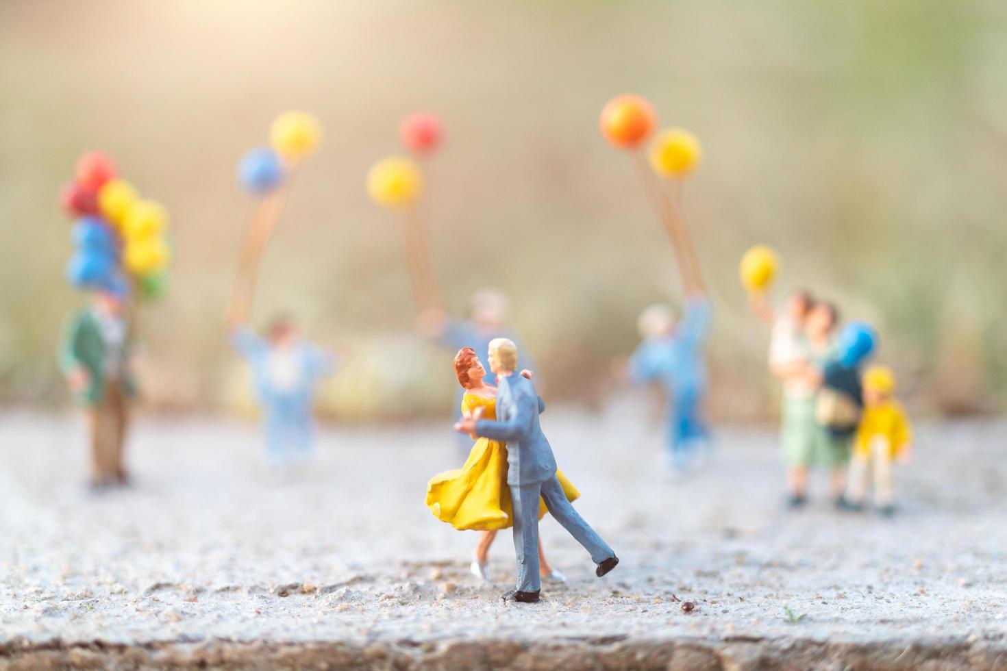 Pareja en miniatura bailando con gente sosteniendo globos en el fondo foto